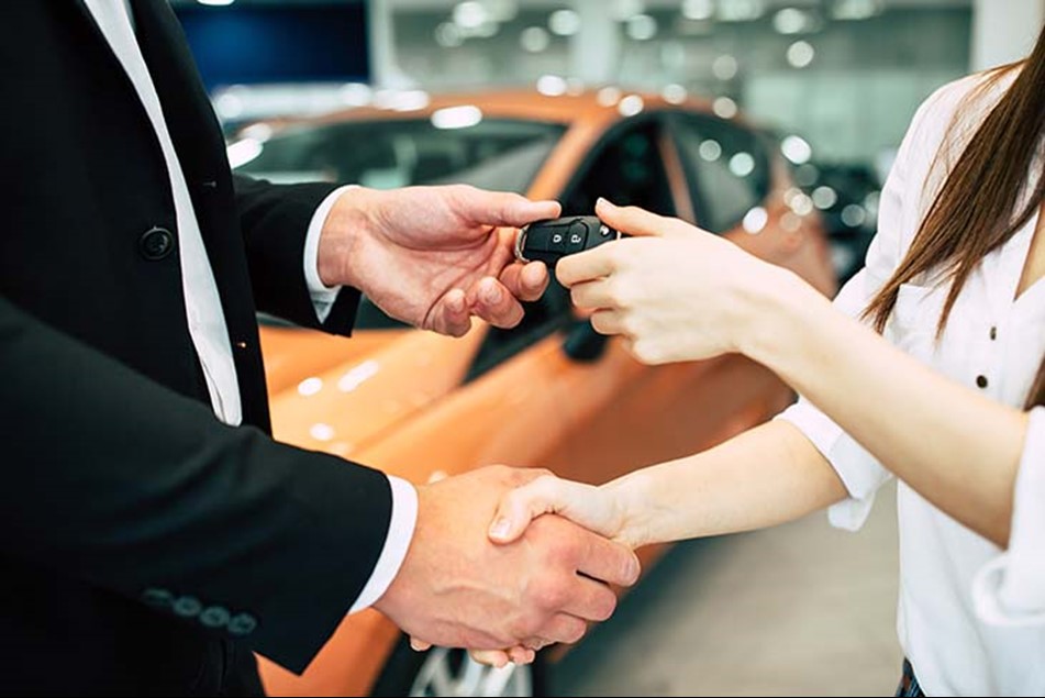 a man shakes hand with a woman and hands her a set of keys completing a car deal